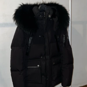 Svart dunjacka från Cedrico - Säljer en snygg svart dunjacka från Cedrico i mycket bra skick. Jackan har en fluffig pälsfodrad huva och praktiska fickor med knappar. Perfekt för kalla vinterdagar med sin varma och stilrena design. Passar både till vardags och festliga tillfällen. Hör av dig vid intresse! 🖤