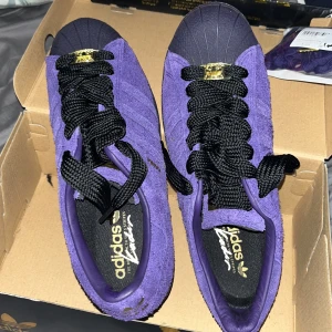 Lila Adidas Superstar i mocka - Snygga lila Adidas Superstar i mocka med klassisk snäcktå och gulddetaljer. Perfekta för att ge din outfit en färgklick. De har en bekväm passform och är idealiska för vardagsbruk. (Dom är nästan helt nya och perfekta ba lite smutsiga i botten finns box och allt med dm för bilder och mer info)