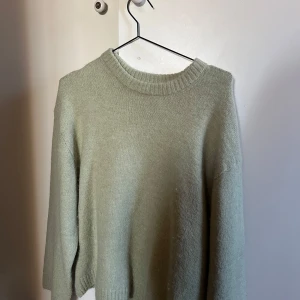 Grön stickad tröja från Gina Tricot - Mysig grön stickad tröja från Gina Tricot i storlek S. Perfekt för kyliga dagar med sin mjuka och varma känsla. Tröjan har en klassisk rund hals och långa ärmar, vilket gör den idealisk för både vardag och mysiga hemmakvällar. Ett måste i garderoben för höst och vinter! Använd en gång!