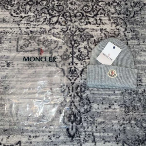 Grå stickad mössa från Moncler - Säljer en snygg grå stickad mössa från Moncler i nytt skick. Den har en broderad logga framtill och är perfekt för kalla dagar. Mössan är mjuk och bekväm, idealisk för både höst och vinter. Kommer med originalförpackning.