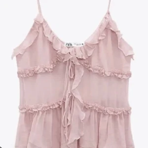 Rosa volanglinne från Zara - Säljer ett supersött rosa linne från Zara med volanger och tunna axelband. Perfekt för sommardagar eller en festlig kväll. Det är luftigt och lätt, vilket gör det idealiskt för varma dagar. Linnet har med knytning framtill💗 