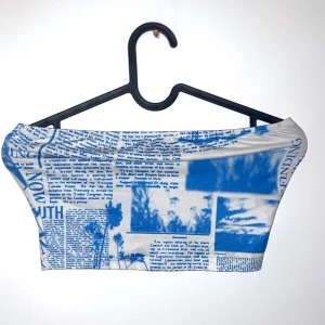 Blå och vit tubtopp med tidningsmönster - Snygg och unik tubtopp i blått och vitt med ett coolt tidningsmönster. Perfekt för sommardagar eller en festlig kväll. Toppen är ärmlös och har en tight passform som framhäver figuren. Ett måste för garderoben om du gillar att sticka ut!