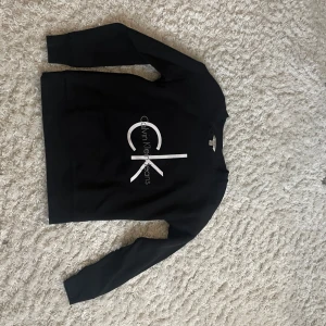 Svart tröja från Calvin Klein Jeans - Säljer en stilren svart tröja från Calvin Klein Jeans i storlek S. Tröjan har ett stort CK-logotryck på framsidan och är perfekt för både vardag och fest. Den är i bra skick och gjord av mjukt material för extra komfort. Säljer pga inte min storlek 