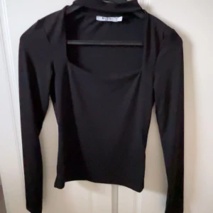 Svart långärmad topp - Snygg svart långärmad topp med fyrkantig urringning från NA-KD . Perfekt för både vardag och fest. Materialet är mjukt och stretchigt vilket ger en bekväm passform. En stilren basplagg som passar till allt!