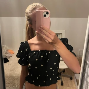 Svart prickig offshoulder topp - Säljer en superfin svart offshoulder topp med vita prickar. Toppen är croppad och har volangdetaljer vid nederkanten. Perfekt för sommaren eller en festkväll! 💫