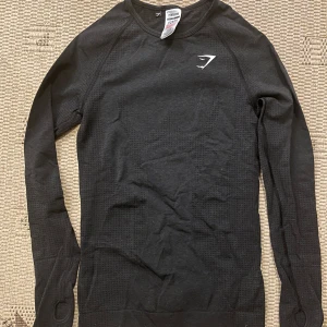 Svart långärmad tröja från Gymshark - Gymshark Vital Seamless 2.0 Long Sleeve Top - Black Marl.  Säljer en svart långärmad tröja från Gymshark i mycket bra skick. Perfekt för träning med sitt stretchiga och bekväma material. Den har tumhål vid ärmsluten för extra komfort. Passar perfekt för höst och vinterträning! OBS Tight modell! (Sista bilden är lånad)