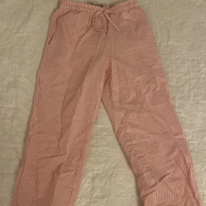 Randiga byxor från Lager 157 - Säljer ett par superbekväma randiga byxor från Lager 157 i modellen Tibby Stripe. De är rosa och vita med en avslappnad passform och dragsko i midjan. Perfekta för en chill dag hemma eller en avslappnad sommarlook. 🩷🤍