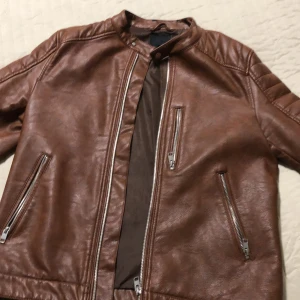 Brun skinnjacka med dragkedjor - Säljer en snygg brun skinnjacka i mycket bra skick. Jackan har en stilren design med dragkedjor på framsidan och vid fickorna. Perfekt för höst och vår, och ger en cool look till vilken outfit som helst. Passar både till vardags och fest! 