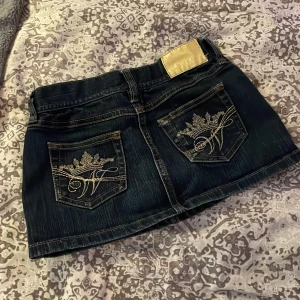 Jeanskjol med broderad ficka - Säljer en snygg jeanskjol i mörk denim med coola broderade detaljer på bakfickorna. Kjolen har en klassisk femficksdesign och en dragkedja fram. Perfekt för en avslappnad sommarlook eller en utekväll med vänner. Passar bra med en t-shirt eller en söt topp!                                          Det här är ai haha men det är i bra skick och så har aldrig använt❤️