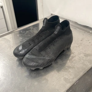 Svarta Nike mercurial fotbollsskor - Säljer ett par svarta fotbollsskor i syntetmaterial. De har en tight passform och är i bra skick, perfekta för fotbollsträning eller match. Skorna har en stilren design med diskreta detaljer och är redo för nya äventyr på planen.