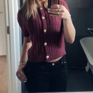 Vinröd kortärmad kofta med knappar - Säljer en superfin vinröd kofta med korta ärmar och snygga guldknappar. Perfekt för både vardag och fest! Den har ett snyggt stickat mönster. Knappt aldrig använd, hör av dig vid intresse! 💖