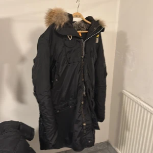 Svart vinterjacka från Parajumpers - Säljer en svart Parajumpers vinterjacka i storlek XXL. Den har en snygg pälsfodrad huva och flera praktiska fickor. Jackan är i mycket bra skick och perfekt för kalla vinterdagar. Den har en dragkedja och knappar för extra skydd mot kyla. Broderad patch på ärmen ger en cool detalj. Jag använder den inte för den är för stor för mig. Pris kan diskuteras 