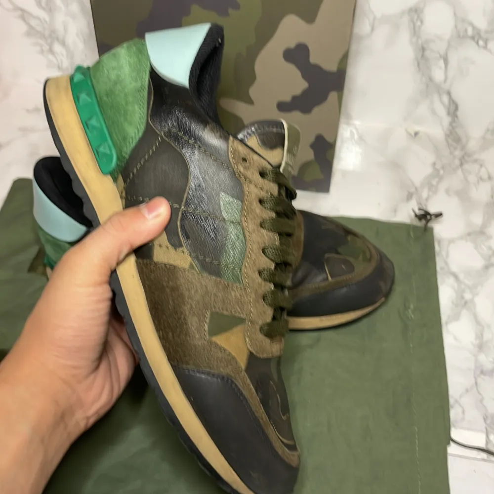 Säljer ett par Valentino Rockrunner sneakers de är i storlek 41men passar 42i camouflage. Skorna har en cool mix av grönt, brunt och svart med detaljer i mocka och skinn. De har en unik design med snörning och en grön häl med nitar. Perfekta för att sticka ut i mängden! . Skor.