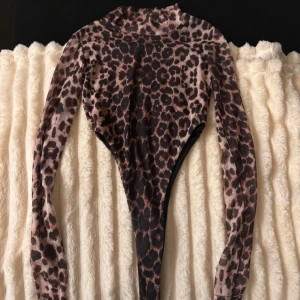 Leopardmönstrad body från PrettyLittleThing - Säljer en snygg leopardmönstrad body från PrettyLittleThing i storlek EU 36. Den har långa ärmar och en tight passform, perfekt för en utekväll eller fest. Materialet är stretchigt och bekvämt. 🐆✨