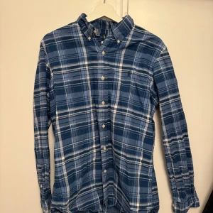 Blå rutig skjorta från Ralph Lauren - Säljer en snygg blå rutig skjorta från Ralph Lauren i storlek M. Skjortan har en klassisk passform med långa ärmar och knappar framtill. Perfekt för både vardag och fest! 💙