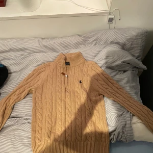 Beige stickad tröja från Ralph Lauren - Säljer en snygg beige stickad tröja från Ralph Lauren. Den har en dragkedja vid halsen och det klassiska logotypbroderiet på bröstet. Perfekt för höst och vinter, och den är i mycket bra skick. Supermysig och stilren!
