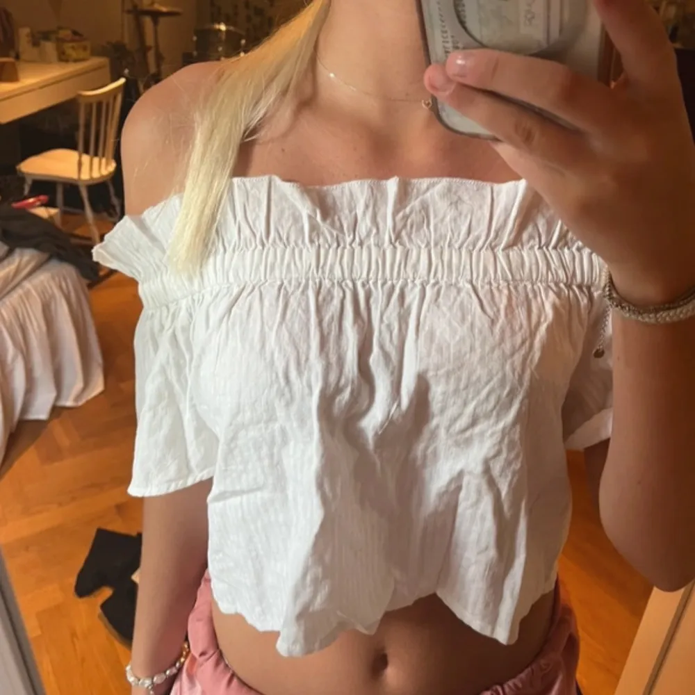 Säljer en superfin vit offshoulder topp i bomull. Den är perfekt för sommardagar med sin luftiga och croppade design. Toppen har en elastisk överdel som ger en bekväm passform och volangdetaljer vid ärmslut och nederkant. Perfekt för en avslappnad och stilren look!. Toppar.