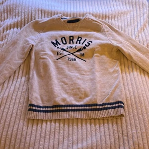 Beige tröja från Morris - Säljer en snygg beige tröja från Morris med tryck framtill. Den har långa ärmar och ribbade muddar i blått och beige vid ärmslut och nederkant. Perfekt för en avslappnad stil! 