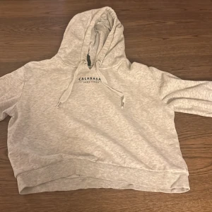 Grå hoodie från H&M - Säljer en snygg grå hoodie från H&M med texten 'Calabasas' tryckt på både fram- och baksidan. Den är lite kortare vid magen. Den är i bra skick och har en skön, lös passform. Perfekt för en avslappnad stil eller mysiga dagar hemma. 🩶
