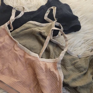 Ribbad topp i flera färger - Säljer tre ribbade toppar i svart, beige och olivgrön. De är ärmlösa med smala axelband och har en croppad passform. Perfekta för sommardagar eller som ett lager under en tröja. Materialet är mjukt och stretchigt för extra komfort.