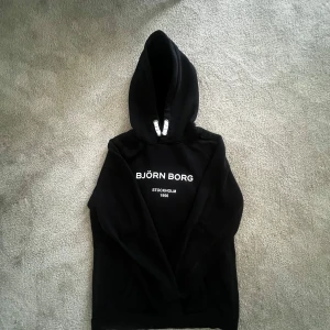 Svart hoodie  - Säljer en stilren svart hoodie från Björn Borg med texten 'Stockholm 1956' på bröstet. Den är använd fåtal gånger 9/10 skick. Perfekt för både höst och vinter. Hoodien har en klassisk passform med bekväm huva. 