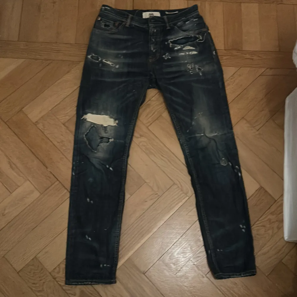 Säljer ett par mörkblå jeans från Taylor Tweed med slitna detaljer och hål för en cool, vintage look. Perfekta för en avslappnad stil. De har en klassisk femficksdesign och är i bra skick trots slitningarna.. Jeans & Byxor.