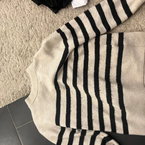 Randig tröja i beige och svart - Säljer en snygg och bekväm randig tröja i beige och svart. Perfekt för både höst och vår. Tröjan har långa ärmar och är gjord i ett mjukt material som känns skönt mot huden. Passar bra till jeans eller kjol för en avslappnad look.