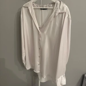 Vit blus från Zara - Säljer en elegant vit blus från Zara i storlek XXL. Blusen har en lös passform med långa ärmar och knappar framtill. Perfekt för både vardag och festliga tillfällen. Materialet känns mjukt och lyxigt, vilket ger en skön känsla mot huden. Passar utmärkt till både jeans och kjol! I silkes liknande material