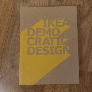 IKEA Democratic Design - En bok med titeln 'IKEA Democratic Design' i en stilren och minimalistisk design. Omslaget är i en naturlig brun färg med en stor gul triangel och text i grått. Perfekt för den som är intresserad av design och IKEA:s filosofi.