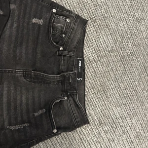Svarta jeansshorts från Summer Denim - Säljer ett par svarta jeansshorts från Summer Denim i storlek S. De är i nyskick och har en cool, sliten look med små revor på fram- och baksidan. Perfekta för sommaren! 🖤