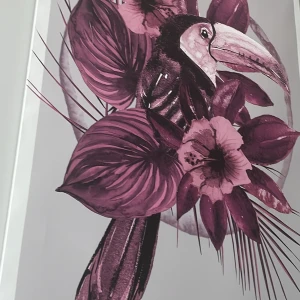 Tavla med fågel och blommor - Säljer en snygg tavla med motiv av en fågel och stora blommor i lila och rosa nyanser. Perfekt för att liva upp vilket rum som helst med lite färg och naturkänsla. Tavlan är inramad och redo att hängas upp på väggen.