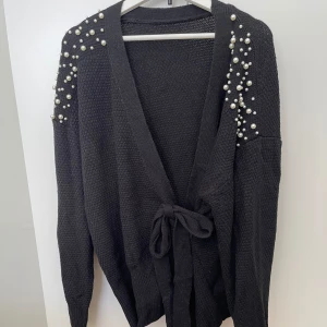 Stickad svart kofta med fina detaljer av pärlor  - Stickad svart kofta från shein i storlek xxl. Detaljer av pärlor som pryder axlarna samt armarna. Aldrig använd så ser ut som ny. 