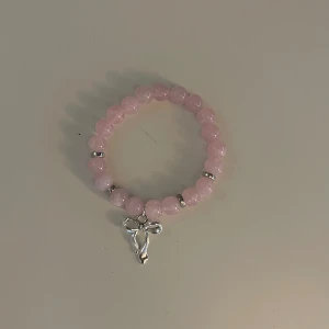Rosa pärlarmband med silverkors - Säljer ett superfint rosa pärlarmband med ett silverfärgat rosätt. Armbandet är elastiskt och passar de flesta handleder. Perfekt accessoar för både vardag och fest! 💖