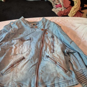 Jeansjacka från Twist & Tango - Säljer en snygg jeansjacka från Twist & Tango i storlek 36. Jackan är ljusblå och har en cool asymmetrisk dragkedja framtill. Den har också flera fickor med dragkedjor och knappar som detaljer. Perfekt för vår och höst! 💙