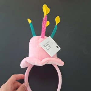 Rosa födelsedagshatt med ljus - Superkul rosa födelsedagshatt som ser ut som en tårta med ljus på toppen. Perfekt för att fira födelsedagar med stil! Hatten är mjuk och bekväm att ha på sig, och ljusen är i olika färger för extra festlig känsla. Passar både barn och vuxna.