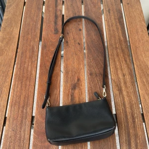 Svart axelväska från H&M - Säljer en snygg svart axelväska från H&M💕Det är en justerbar axelrem och ett extra fack💕Perfekt för både vardag och fest💕Skicket är jättebra💕Pris kan diskuteras💕