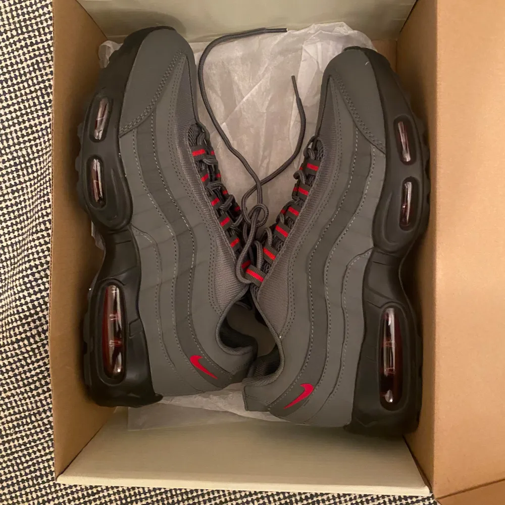 Säljer ett par gråa Nike Air Max sneakers 95 i storlek 43. Skorna har en snygg design med röda detaljer och är i nyskick. De har en bekväm passform och är perfekta för både vardag och träning. Sulan är svart med synliga luftkuddar för extra komfort. Pris kan diskuteras vid snabb affär. Kengät.