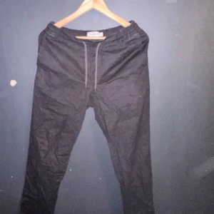 Svarta linnebyxor från Dressmann - Säljer ett par svarta linnebyxor från Dressmann i storlek XS. Byxorna har en elastisk midja med snörning för extra komfort och två bakfickor med knappar. Perfekta för en avslappnad stil eller sommarens varma dagar. 