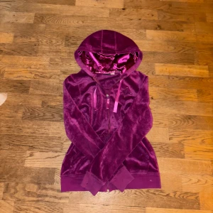 Lila sammetshoodie med dragkedja - Säljer en supermjuk lila hoodie i sammet med dragkedja framtill. Den har en snygg broderad detalj på bröstet och en mysig huva med satinband. Perfekt för höst och vinter när du vill vara både bekväm och stilren. Passar lika bra till vardags som till en chill kväll med vänner. 💜