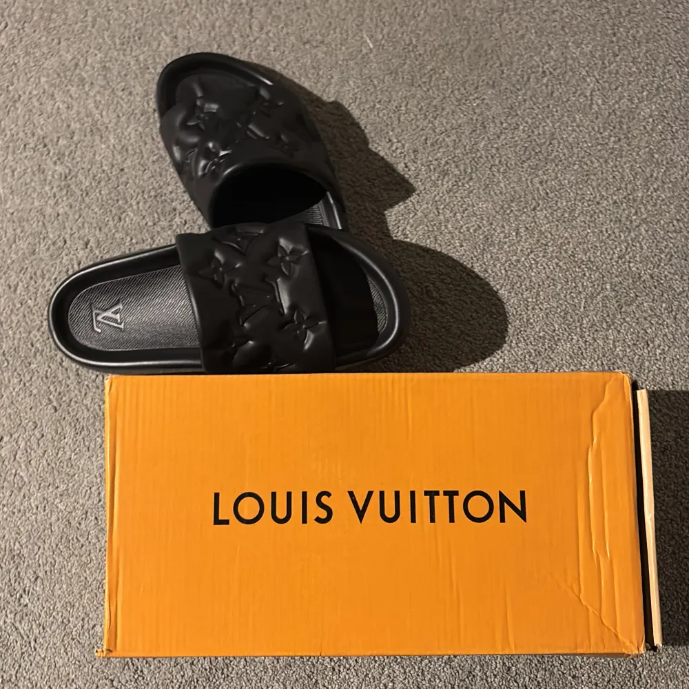 Säljer ett par svarta Louis Vuitton Waterfront Mule sandaler i nytt skick. De har en stilren design med det klassiska LV-mönstret präglat på ovandelen. Perfekta för sommarens alla äventyr eller bara för att chilla hemma. Kommer i originalförpackning.. Skor.