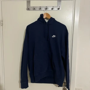 Mörkblå hoodie från Nike - Säljer en snygg mörkblå hoodie från Nike i storlek L. Den har en klassisk design med en liten vit Nike-logga på bröstet och en praktisk magficka. Perfekt för både vardag och träning. Huvan har dragsko för justerbar passform. Skön och stilren!