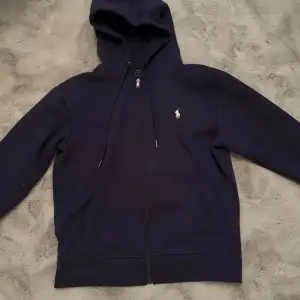 Säljer en snygg marinblå hoodie från Ralph Lauren i storlek S. Den har en dragkedja framtill och en klassisk broderad logga på bröstet. Perfekt för både höst och vår, och passar till alla tillfällen. Grymt skön och stilren! OBS: den är lite solbränd vilket är därför jag säljer så billigt men den är köpt från Polo Ralph Lauren