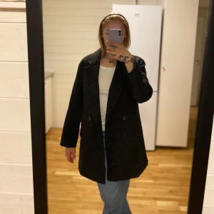 Svart kappa Lager157 - Säljer en stilren svart kappa i bra skick. Den har en klassisk design med långa ärmar och en rak passform. 