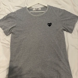 Grå t-shirt från Comme des Garçons - Säljer en stilren grå t-shirt från Comme des Garçons med det ikoniska svarta hjärtat på bröstet. T-shirten sitter som S, skriv vid några funderingar!