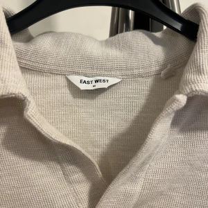 Beige tröja från East West - Säljer en stilren beige tröja från East West i storlek M. Tröjan är långärmad och har en klassisk krage. Använd endast 2 gånger, sedan krympte den något i tvätten. Passar därför troligen bättre som S än M
