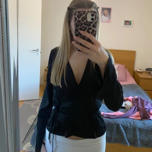 Svart omlottopp från BikBok - Snygg svart omlottopp från BikBok i storlek XS. Toppen har långa ärmar och ett knytband i midjan för en smickrande passform. Perfekt för både vardag och festliga tillfällen. 🖤