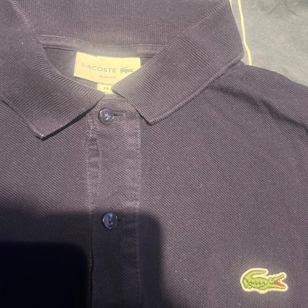 Säljer en klassisk mörkblå pikétröja från Lacoste med den ikoniska krokodilloggan på bröstet. Nått år gammal därav billigt pris, hör av er för fler frågor. T-paidat.