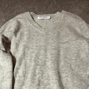 Grå kashmirtröja från Eos Stockholm Luxury Cashmere - Säljer en lyxig grå kashmirtröja från Eos Stockholm. Tröjan har en v-ringad design och långa ärmar, perfekt för kyligare dagar. Den ribbade kanten ger en stilren look. Passar både till vardags och mer uppklädda tillfällen.