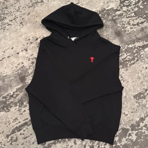 Svart Ami Paris Hoodie  - Snygg svart hoodie från Ami Paris. Perfekt för en avslappnad stil. Den har en klassisk huva med dragsko och ribbade muddar vid ärmslut och nederkant.
