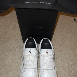 Vita sneakers från Giuseppe Zanotti - Snygga vita sneakers från Giuseppe Zanotti med dragkedja och snörning. Skorna är i otroligt bra skick och knappt använda den jag köpte dessa i mitten av oktober.  Skorna är helt äkta och köpta från farfetch.com för mer frågor skriv i dm